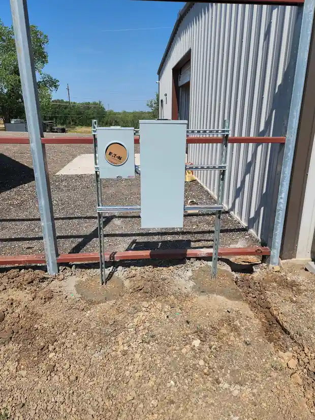 New meter base and disconnect on a galvanized rack beside a steel building