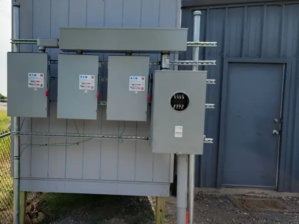 Meter and four disconnects mounted on a commercial metal building behind chain link