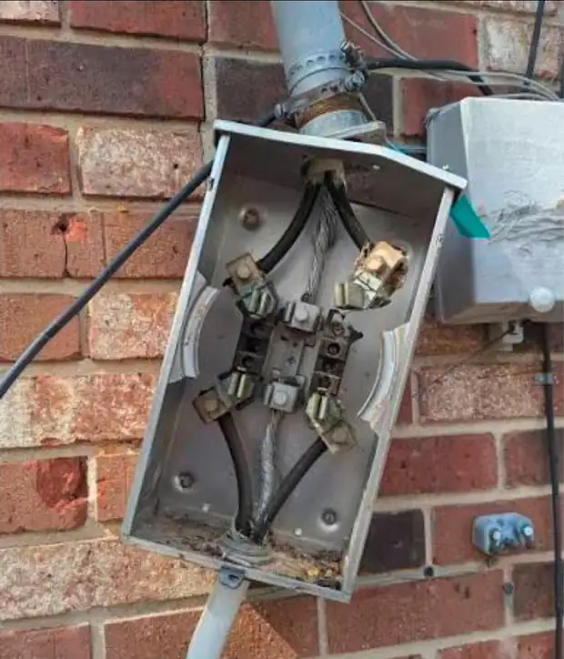 An opened, corroded meter base on a brick wall before repair