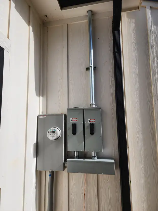 Meter base and two disconnects with a conduit riser on a wood-sided wall